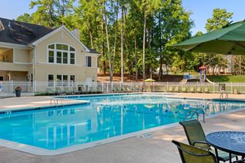 Leasing office exterior with swimming pool and sun deck with lounge chairs with trees and building exteriors in the background